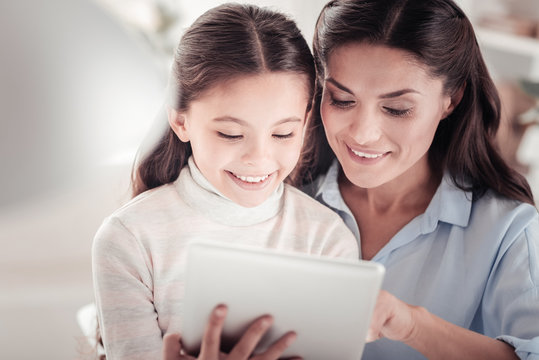 Positive charismatic girl playing tablet games with mother at home