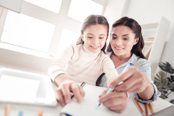 Progressive good-looking mother helping her talented girl drawing