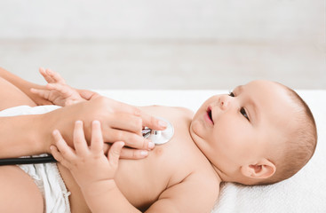 Doctor examining little baby with stethoscope in clinic.