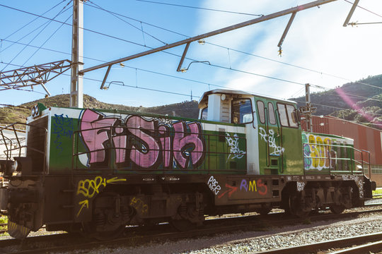 Old green train locomotive, painted in graffiti. In a train station in Spain.