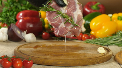 Chef in black gloves takes a steak marinated olive, a sprig of rosemary, a clove of garlic and a mixture of peppers water all abundant olei, in the background vegetables, the background is blurred