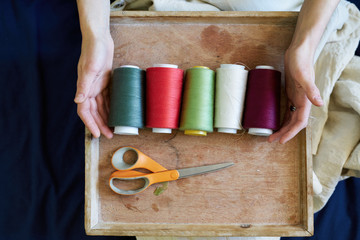 Seamstress or dressmaker keeps colorful spools of thread in hands on wooden background, top view.