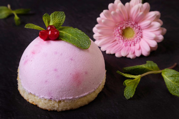 Pink round berry cake on a dark background, in the background flowers