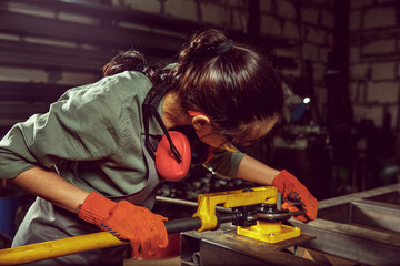 Busy and serious craftswoman grinding timbers with special machine. Beautiful woman wearing safety...