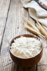 Flour in wooden bowl and wheat ears on wooden background. Copy space.