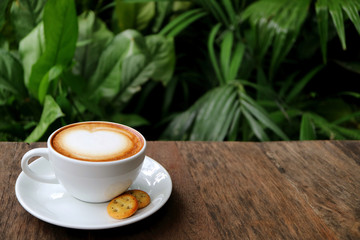 Cup of Hot Cappuccino Coffee with Cookies Served on Wooden Table with Blurry Green Foliage in Background