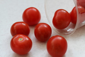 Several red ripe cherry tomatoes rolled out of a plastic transparent glass