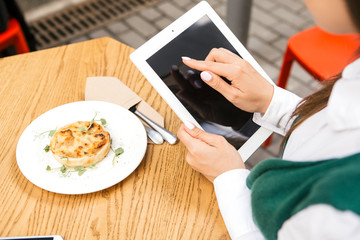 Brunette business woman working as a freelancer from a cafe in summer terrace. She drinks tea and use gadgets as laptop and tablet and phone for her work. Space for text. Top view from above