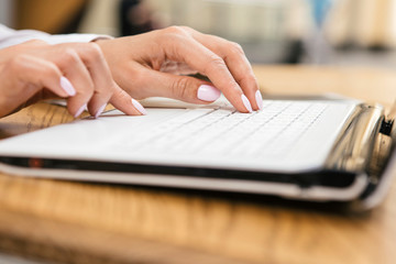 Woman typing on a laptop keyboard in a warm sunny day outdoors, sitting at the cafe table. Space...