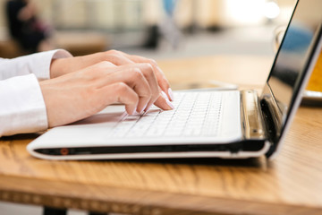 Woman typing on a laptop keyboard in a warm sunny day outdoors, sitting at the cafe table. Space...