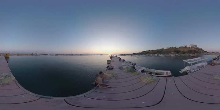 NEA KALLIKRATIA, GREECE - AUGUST 12, 2017: 360 VR video. Boats and yachts at anchor in quay. Marine scene at sunset. Dad and son (with model release) sitting on the pier with fishing nets, tourist