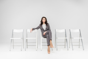 attractive woman sitting with crossed legs on chair isolated on grey