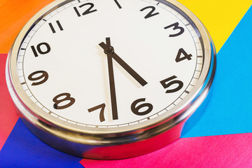 Steel clock on a multicolored background, the hands show half of the sixth. Close up. The view from...