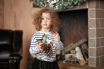 little girl with a pine cone standing by the fireplace on Christmas eve