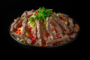 A plate of delicious rice with beef and vegetables: carrots, sweet peppers, greens, spices and sauce on a black background