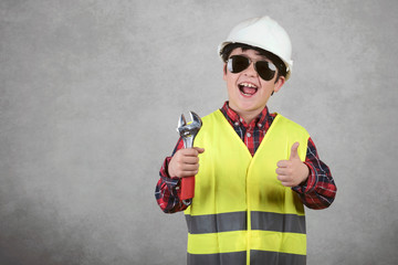 little child construction worker in White helmet and sunglasses and holding a wrench