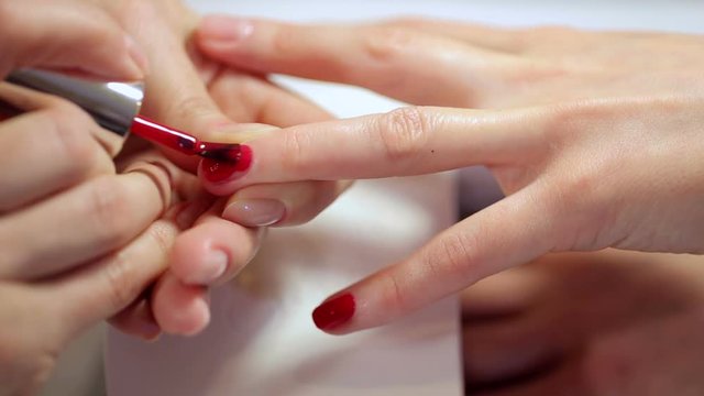 Woman nail master doing nails to a girl client at a beauty salon. A beautician applies red nail polish to a young womans nails. The concept of nail care.