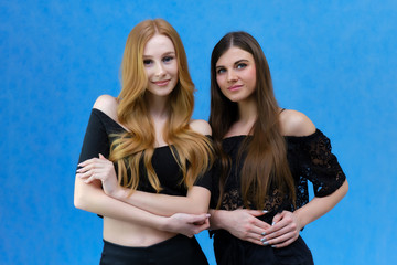 A concept portrait of two cute beautiful girls talking on a blue background in the studio