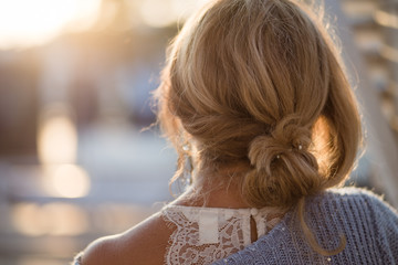 Back view of a woman with tied blond hair looking at the sunset. Woman in blue knitwear.