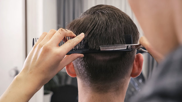 back view of female barber haircut doing male hair style.