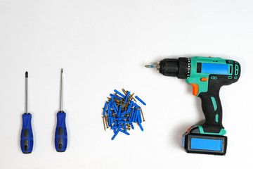 Top view of arranged drill with screwdrivers and pile of nails on white background