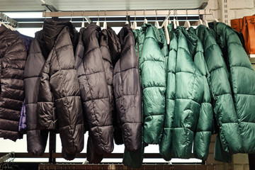 Rack with trendy warm coats of green and black colors in clothes shop.