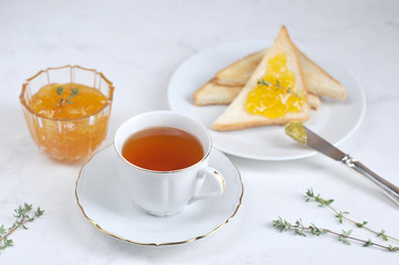 Toasts, orange jam and a cup of tea. The concept of table setting for breakfast. Light background. Close-up.