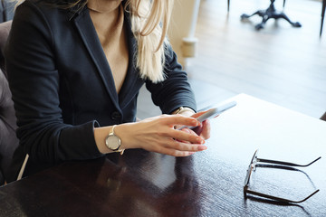 unrecognizable blonde business woman in suit with phone sitting at a table in a cafe, close up