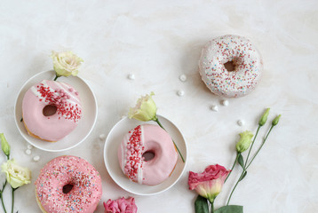 Flat lay composition with pink donuts and flowers on a bright background