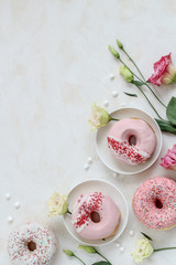 Flat lay composition with pink donuts and flowers on a bright background
