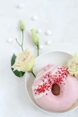 Flat lay composition with a pink donut and flowers on a bright background