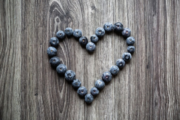 Ripe tasty blueberries and berries on a wooden table in the shape of heart