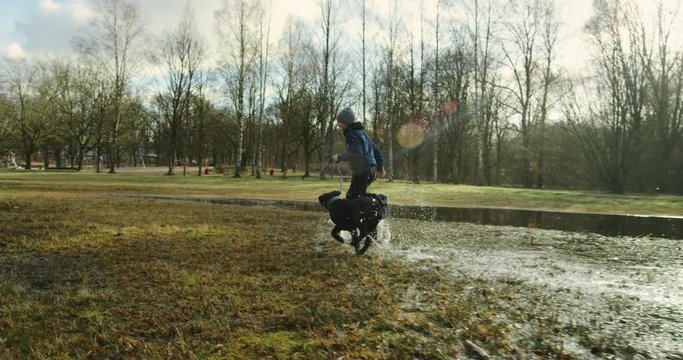 Happy boy and his young dog running through puddles in a park