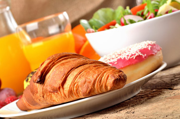 Detail of croissant, orange juice and fresh salad - breakfast on wooden table
