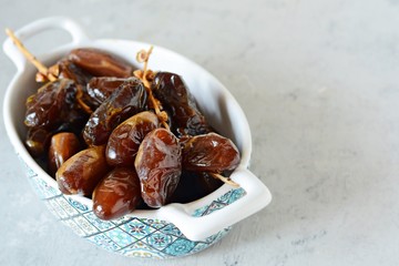 Bowl with juicy dates on a branch on a gray-blue background. Healthy tasty food. Raw Organic Medjool Dates 