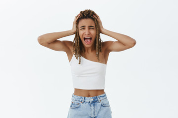 Girl going insane. Portrait of panicking emotive dark-skinned woman overreacting screaming from panic and shock holding hands on dreadlocks yelling displeased, feeling perplexed and concerned