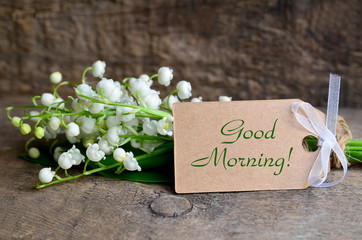 Naklejka premium Bouquet of fresh lily of the valley flowers and tag card with a Good Morning inscription on old wooden table.Beautiful spring still life concept.Selective focus.