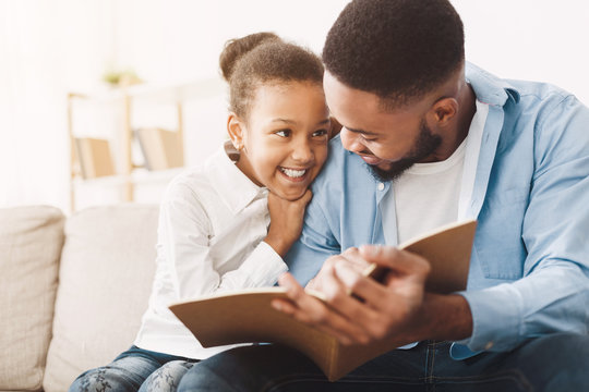 African-american dad and daughter spending time, reading book