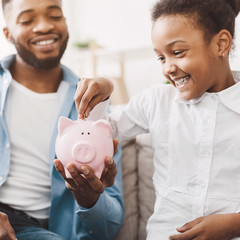 Pretty girl putting coin into piggybank with father