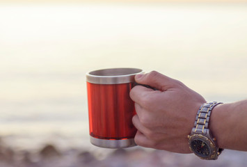 A man's hand holds a cup of coffee against the background of the sea