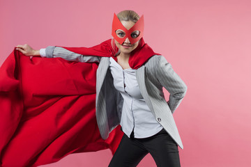 Young attractive woman superhero. Girl in a business suit and a mask with red cloak of hero.