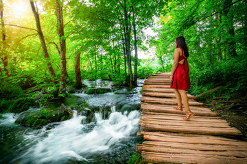Woman traveler walking on wooden path trail with lakes and waterfall landscape in Plitvice Lakes...