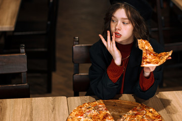 Beautiful young curly girl in black hat with piece of pizza