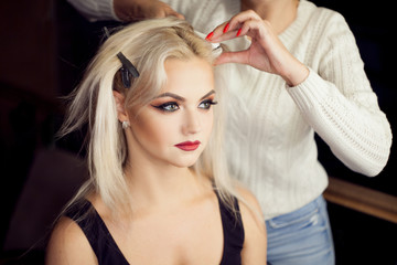 Fototapeta premium Beautiful young blonde. Makeup artist makes hair.