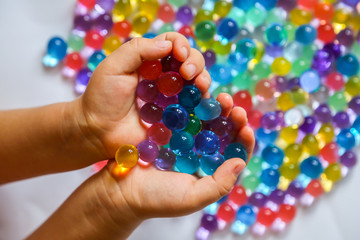 Colored balls of hydrogel in child's palms. Sensory experiences - obrazy, fototapety, plakaty