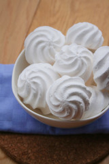 Small white meringues in a bowl on wooden table