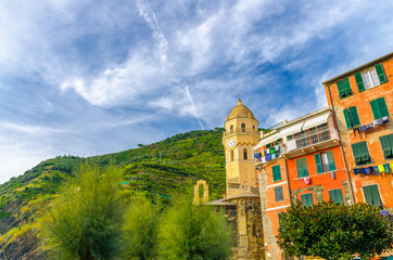 Chiesa di Santa Margherita di Antiochia church and colorful building in Vernazza village, blue sky with transparent white clouds background, National park Cinque Terre, La Spezia, Liguria, Italy