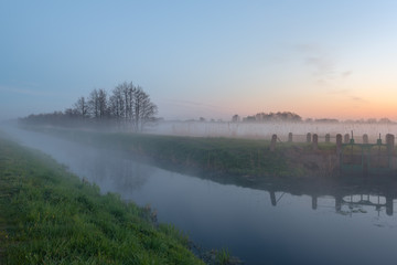 Mysterious foggy evening in a field near the river at the sunset time. Karwia village in Poland.