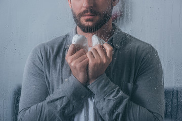 cropped view of man holding baby shoes through window with raindrops