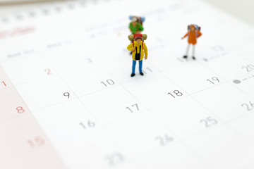 Miniature people, travelers standing on the calendar, mark date for traveling to destination. Used in the travel business concept.